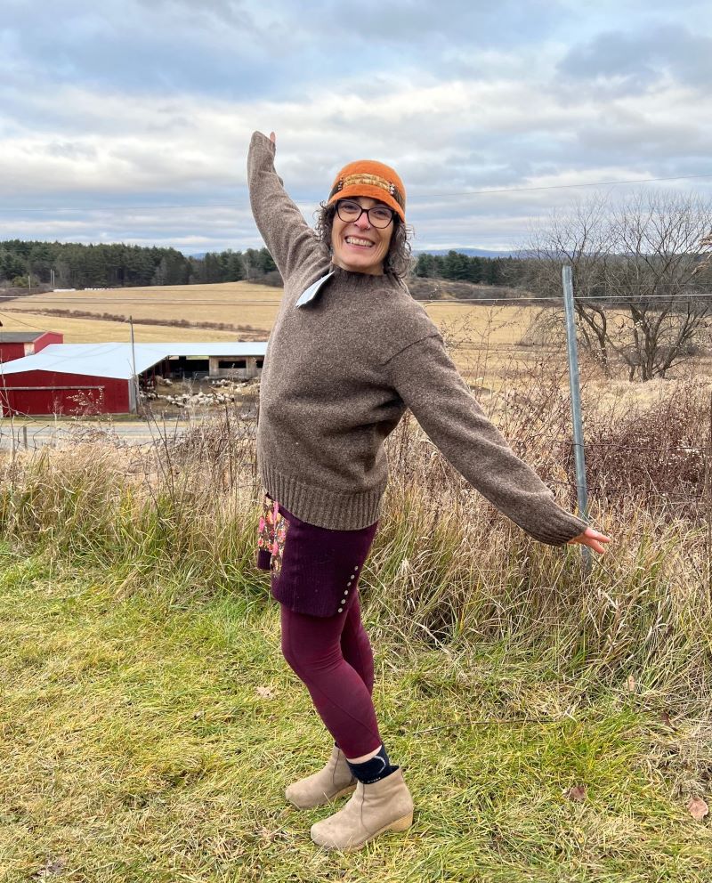 Woman models a wool sweater while standing in a field on a farm