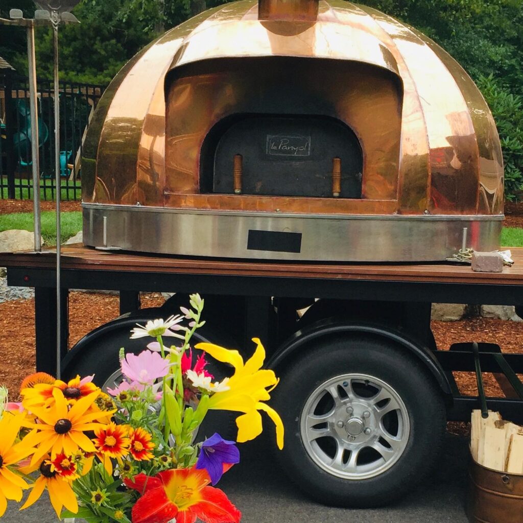 Fresh flowers in front of a copper-clad wood-fired pizza oven.